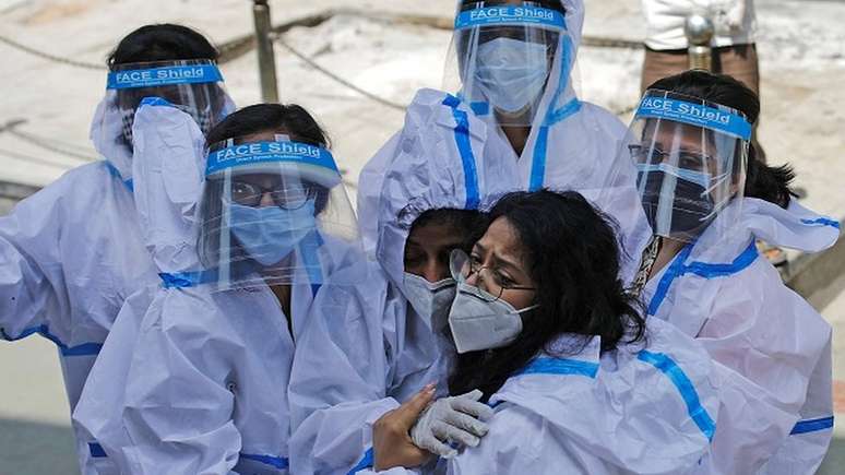 Grupo de trabalhadoras da saúde com equipamento de proteção individual se abraça