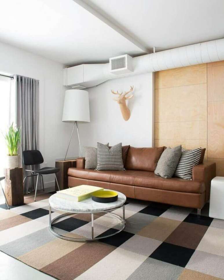 63. Sofá de couro com almofadas para sala de estar decorada com tapete quadriculado e mesa de centro redonda – Foto: Houzz