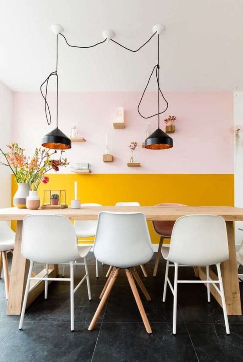 31. Pintura meia parede amarela para sala de jantar decorada com mesa de madeira e luminária pendente preta – Foto: Pinterest