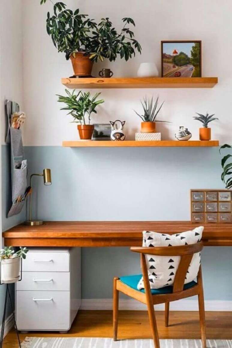 32. Pintura meia parede azul pastel para home office decorado com escrivaninha de madeira e vasos de plantas – Foto: Jeito de Casa