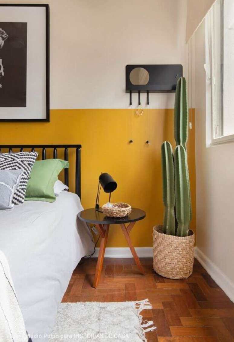 50. Decoração meia parede amarela para quarto com cabeceira preta e vaso de chão – Foto: Histórias de Casa