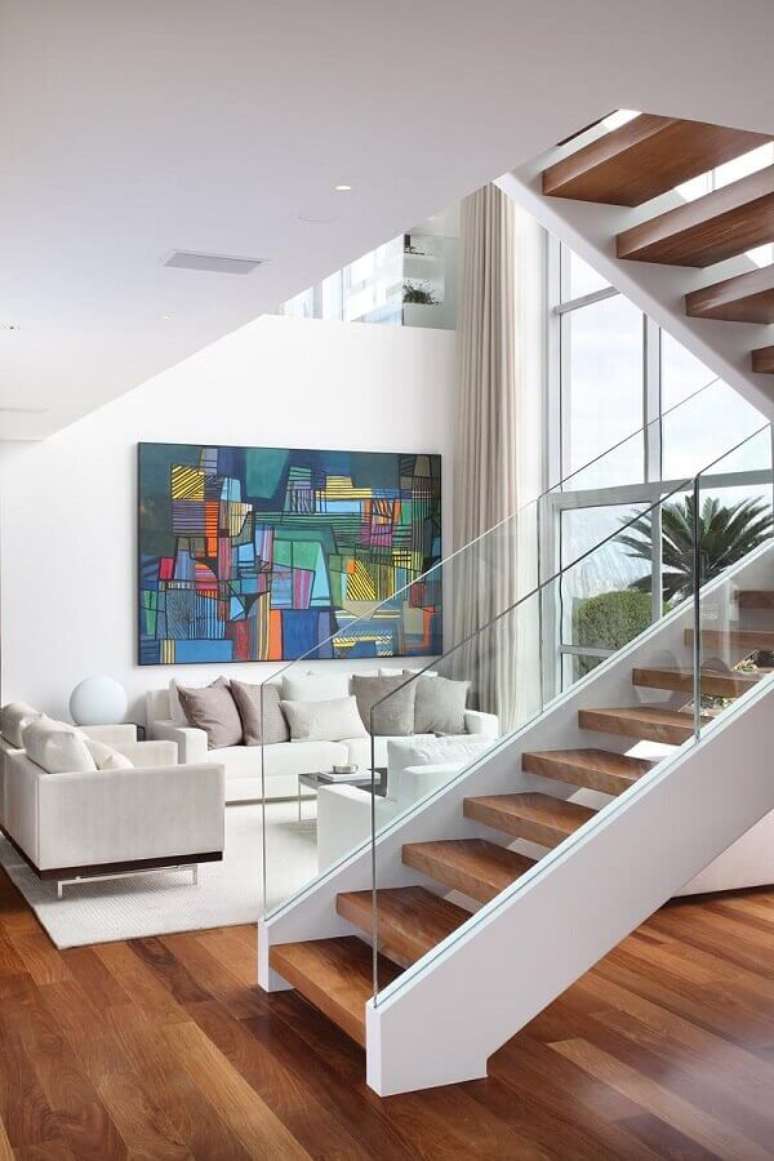 58. Sala branca decorada com quadro colorido e escadas internas vazada com degraus de madeira – Foto: A1 Arquitetura