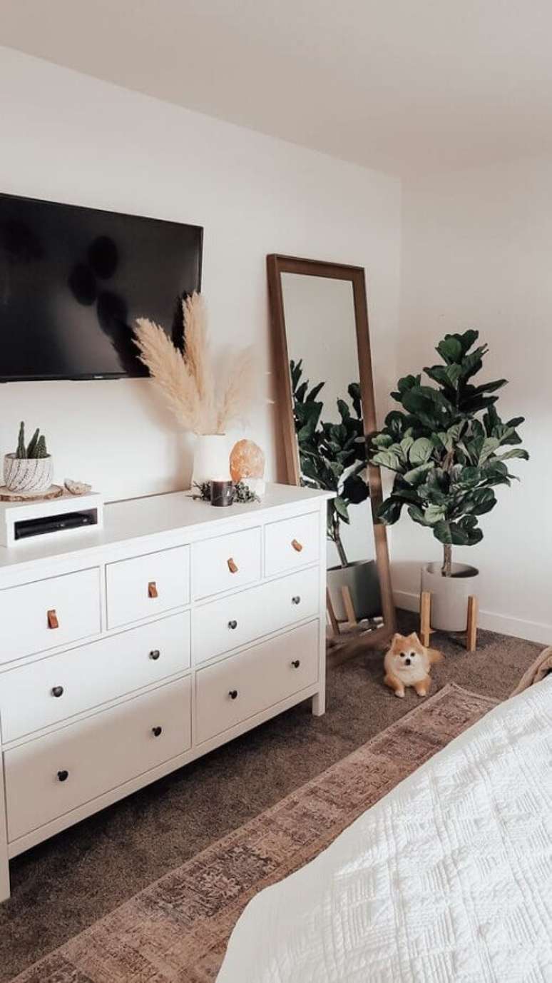 17. Cômoda branca para quarto decorado com espelho de chão e planta grande – Foto: Pinterest