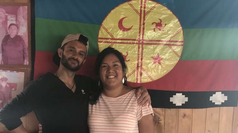 Maria e Daniel posando com uma bandeira mapuche. Maria lamenta ter demorado para descobrir que &eacute; quase 100% ind&iacute;gena