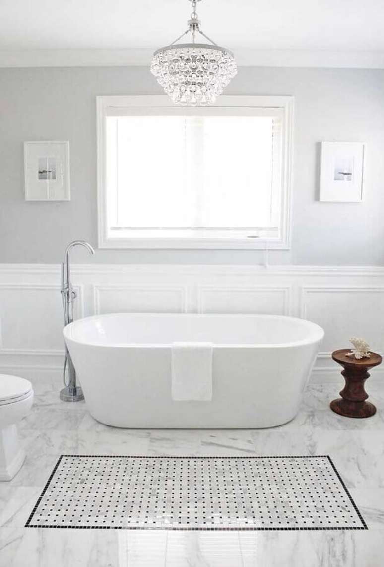 14. Banheiro branco com banheira decorado com lustre de teto de cristal – Foto: