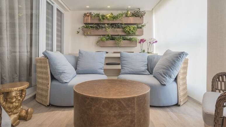 6. Varanda com sofá em tons neutros, mesa de canto dourada e floreira de madeira. Projeto por Marli Assis