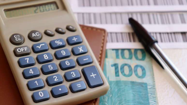 Calculadora, notas de R$100, caneta e boletos