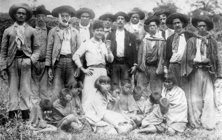 Em pé, bugreiros posam com mulheres e crianças do povo Xokleng capturadas após ataque a acampamento.