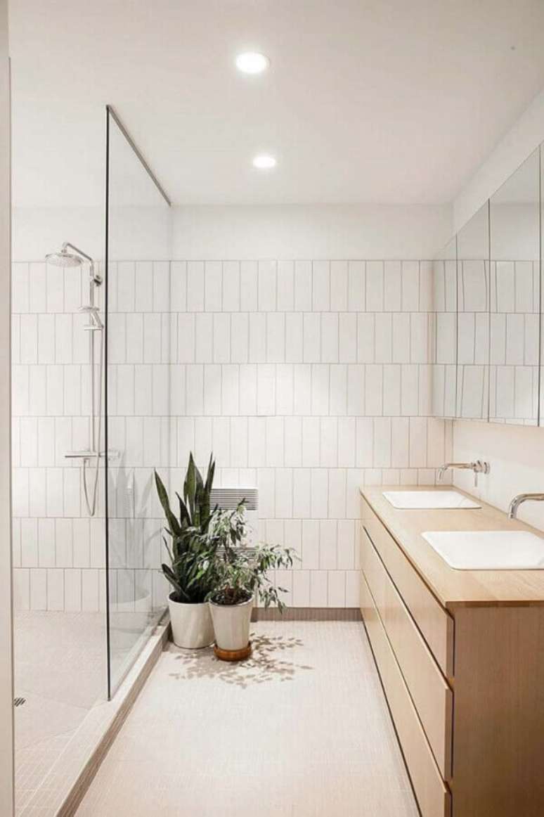 16. Banheiro com gabinete de madeira e revestimento cerâmico branco. Fonte: HomeDeco