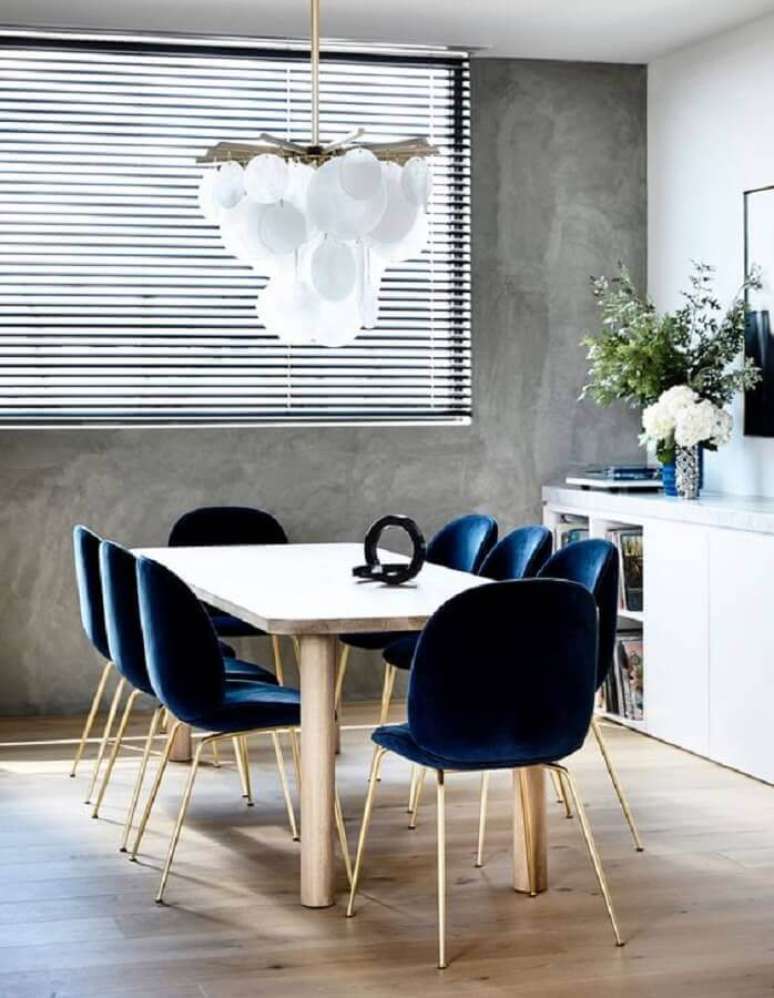 39. Decoração de sala de jantar com parede de cimento queimado e cadeira estofada azul marinho – Foto: The Design Files
