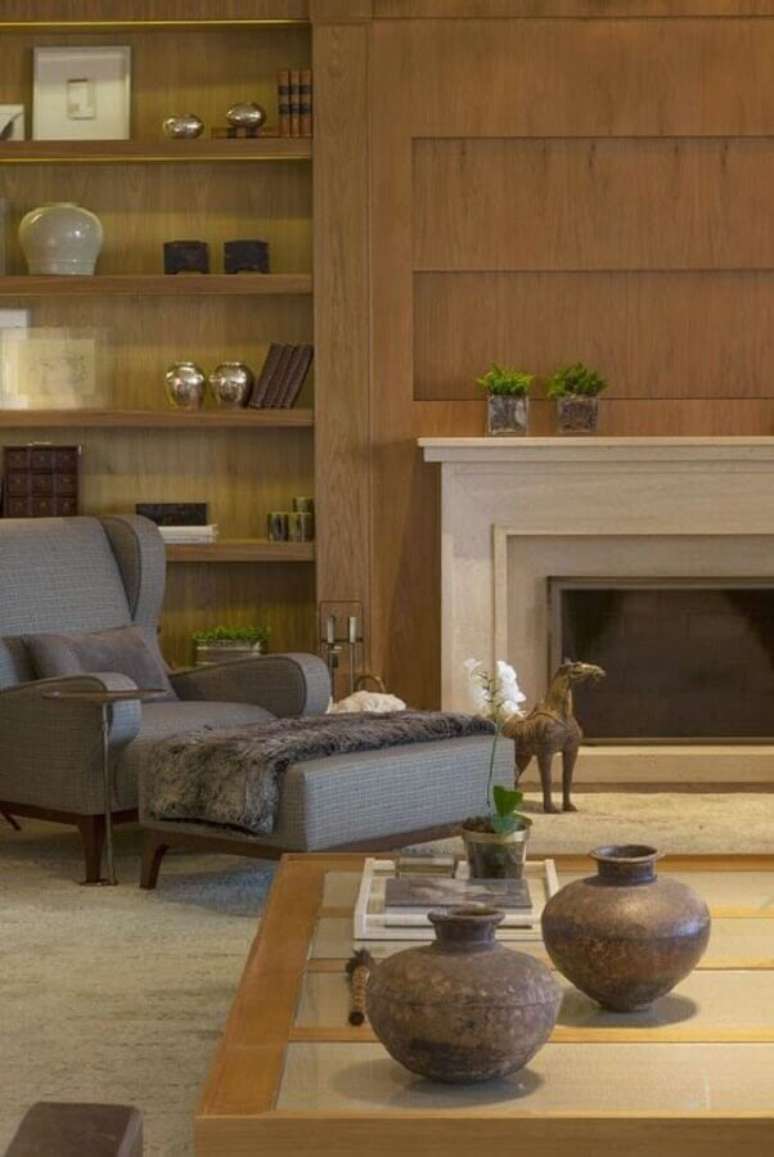 46. Sala com lareira decorada com poltrona cinza e prateleiras de madeira – Foto: Casa Tres Chic