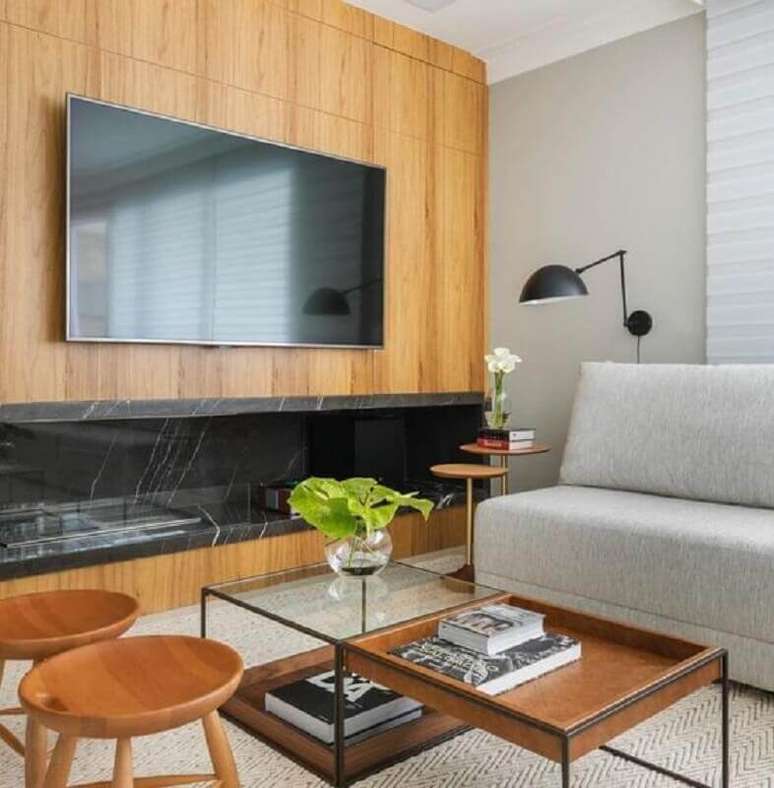 48. Sala com lareira grande decorada com sofá cinza sem braço e revestimento de madeira – Foto: Pinterest