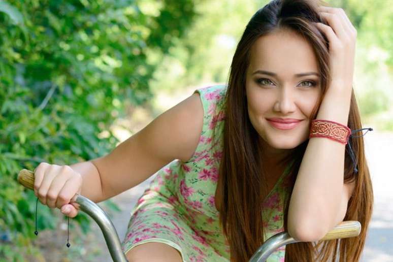 Mulher com vestido floral, encostada na bicicleta e sorrindo - FOTO: Shutterstock Images