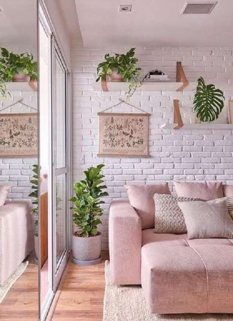 37. Sala de estar com parede de tijolinho e sof&aacute; rosa claro retr&aacute;til. Fonte: Pinterest