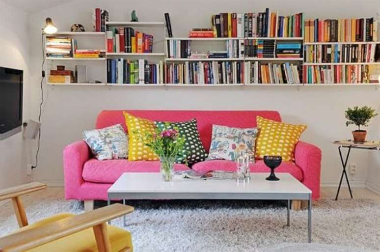 40. Sala de estar com prateleiras para livro e sof&aacute; rosa. Fonte: Pinterest