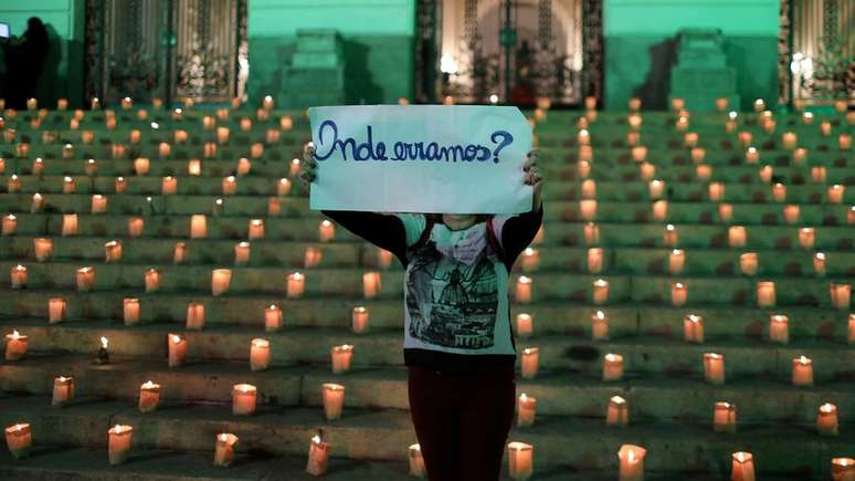 Manifestante, com velas ao fundo, segura cartaz, onde está escrito: "Onde erramos?"