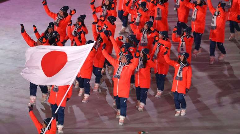 Atletas olímpicos com bandeira do Japão enquanto apresentam delegação