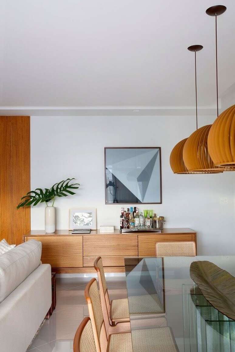20. Buffet de madeira para sala de jantar decorada com mesa de vidro e lumin&aacute;ria redonda de madeira &ndash; Foto: Casa de Valentina