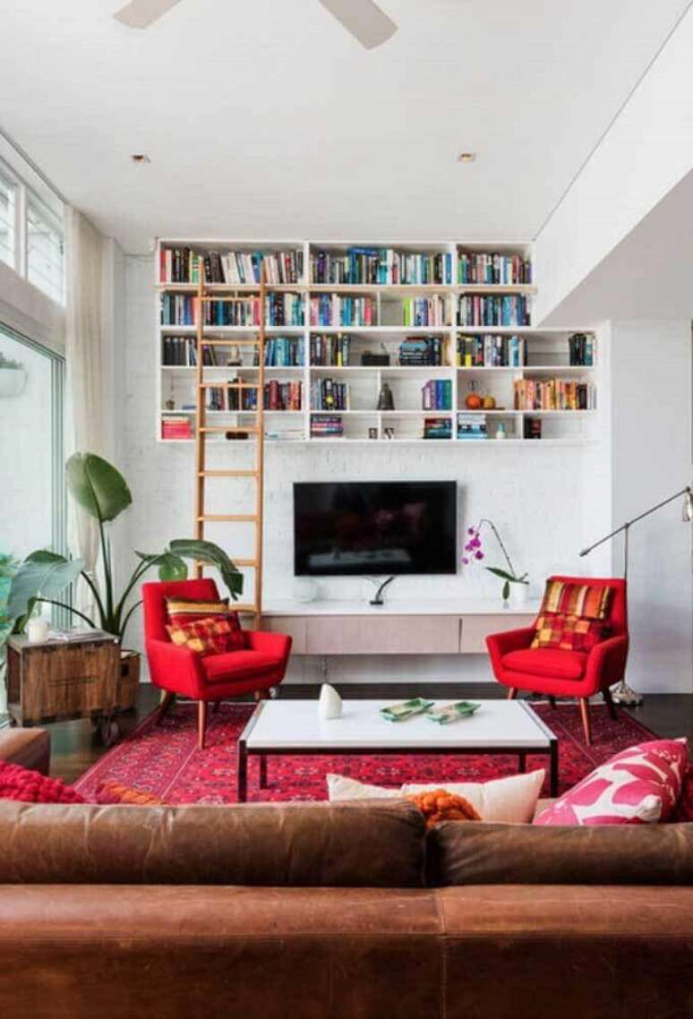 63. Poltrona vermelha para sala decorada com sofá de couro e nichos para livros – Foto: Jeito de Casa