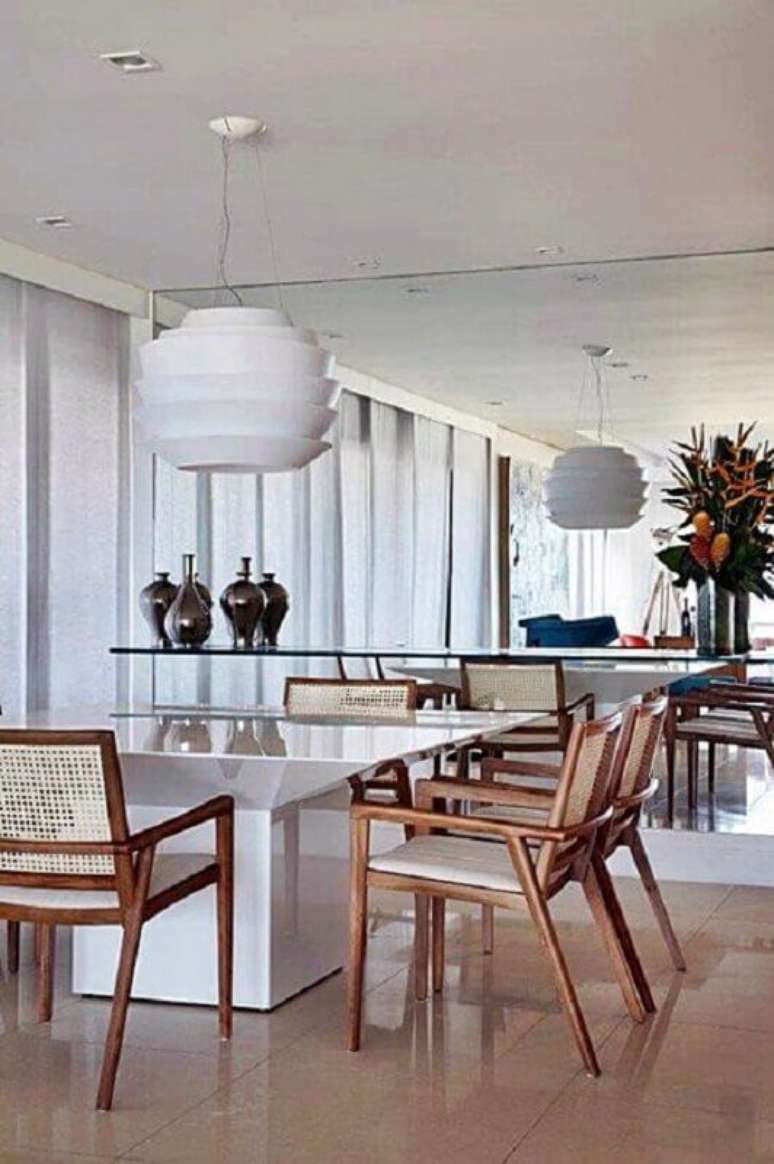 43. Luminária para sala de jantar branca decorada com parede espelhada e cadeiras de madeira – Foto: Simples Decoração