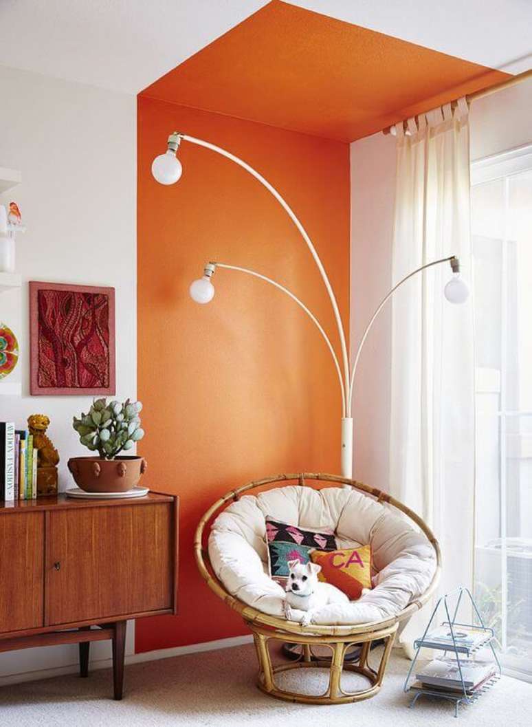 3. Parede de sala decorada com pintura setorizada laranja perto do rack de madeira e poltrona de ratan – Foto Pinterest