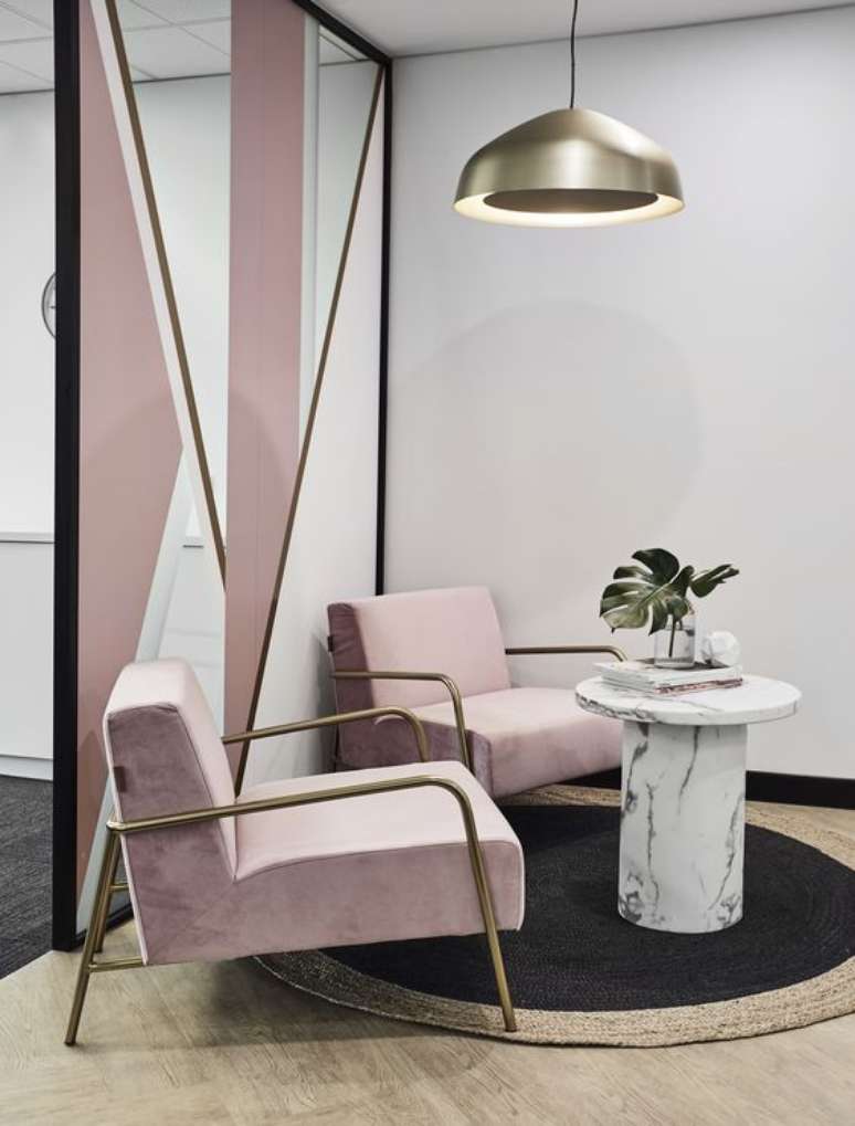 55. Sala de espera com poltronas cor de rosa e mesa de centro marmorizada com revistas e vaso de plantas – Foto Morphos Projects