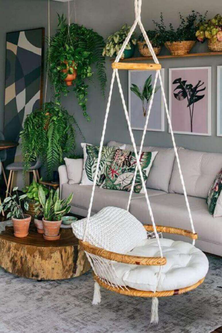 2. Cadeira de balanço suspensa para sala cinza decorada com vasos de plantas e mesa de centro rústica – Foto: Pinterest
