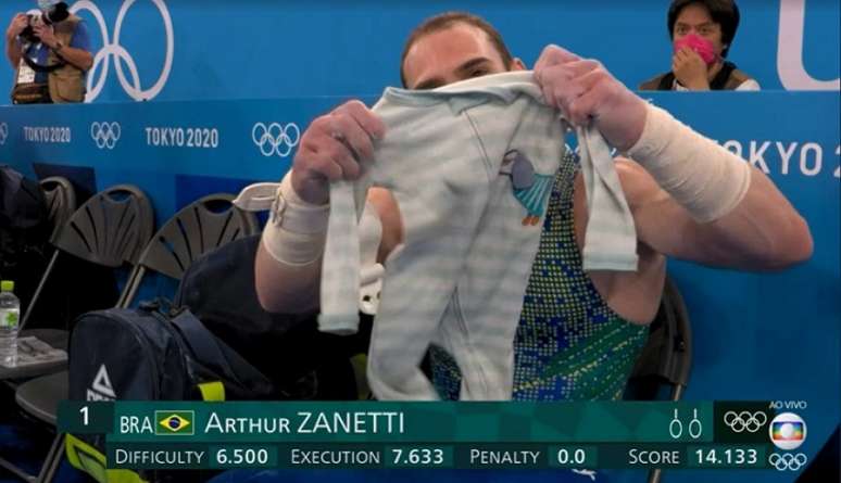 Zanetti mostra o 'amuleto' durante os Jogos, uma roupinha do filho Liam (Foto: Reprodução/Globo)