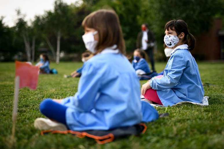 crianças sentadas na grama com máscara e distanciamento