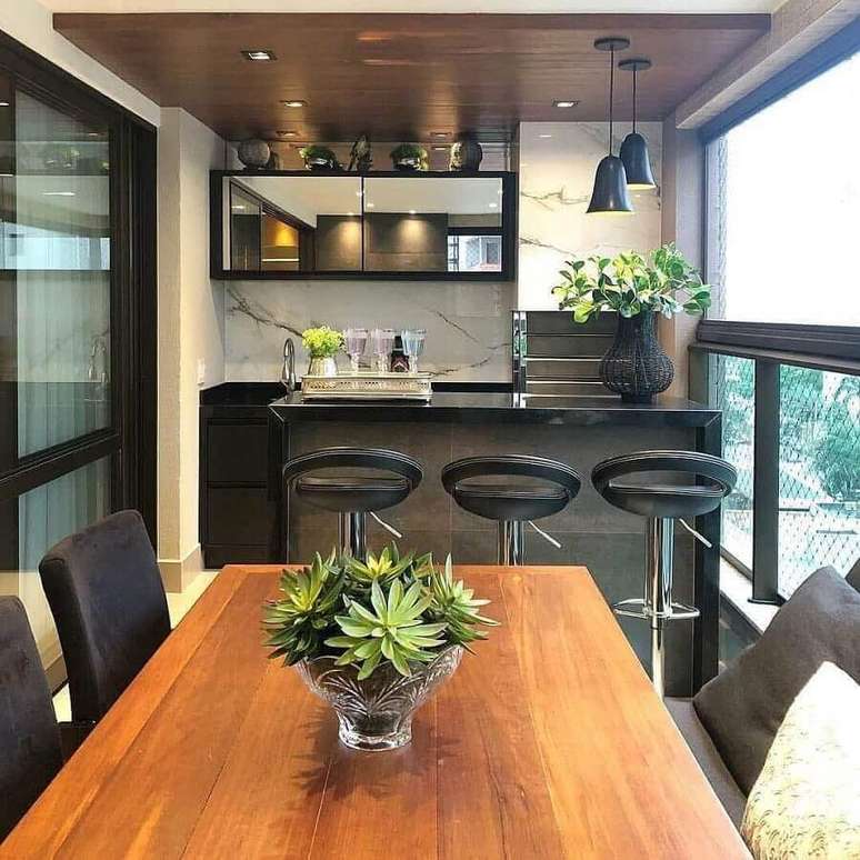 14. Apartamento com varanda gourmet e churrasqueira decorada com mesa de madeira e banqueta preta – Foto: Jeito de Casa