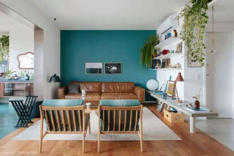 2. Sala azul e branca decorada com sofá cor caramelo e poltrona de madeira – Foto: Jeito de Casa