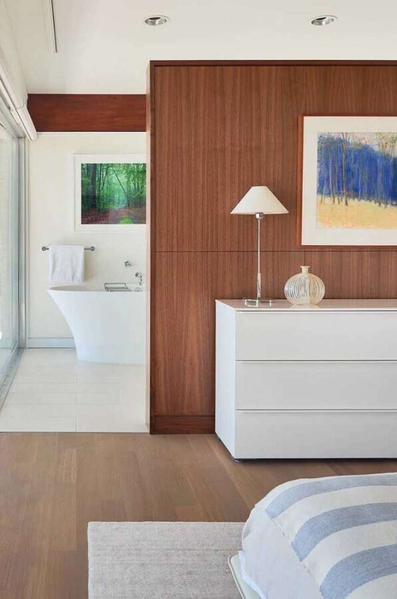 27. Cômoda branca para quarto suite decorado com parede de madeira – Foto: Jeito de Casa