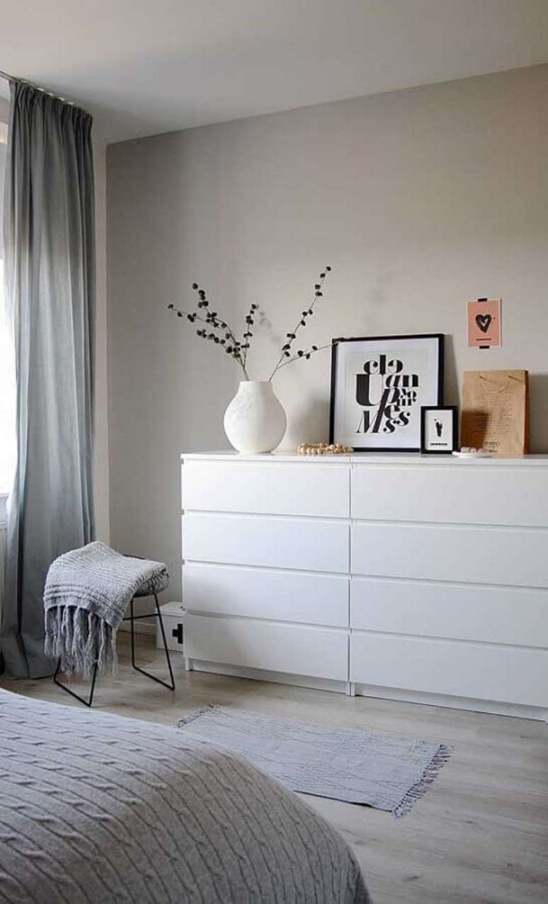 24. Cômoda branca para quarto de casal minimalista decorado com cortina cinza e piso de madeira clara – Foto: Apartment Therapy