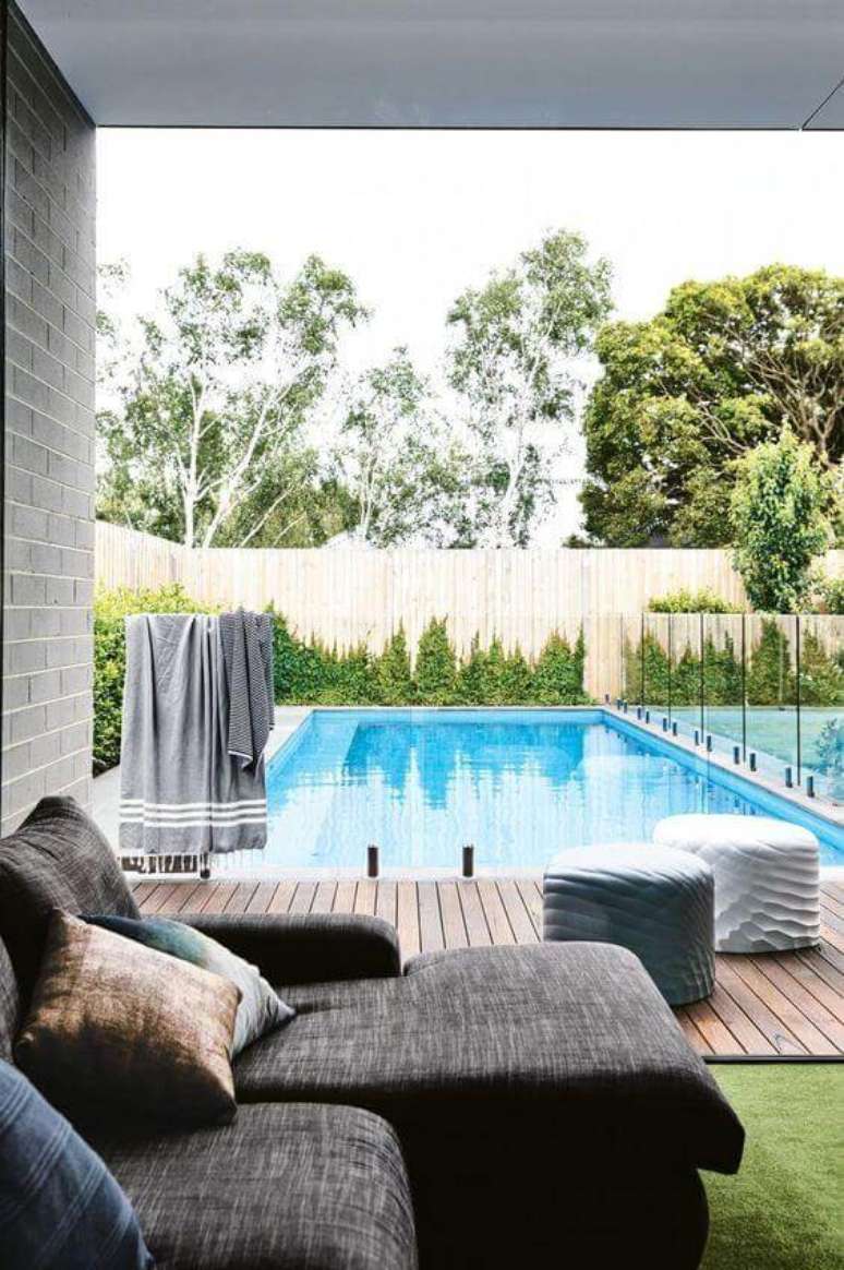 37. Área gourmet com sofá cinza confortável perto das piscinas modernas e deck de madeira – Foto Pinterest