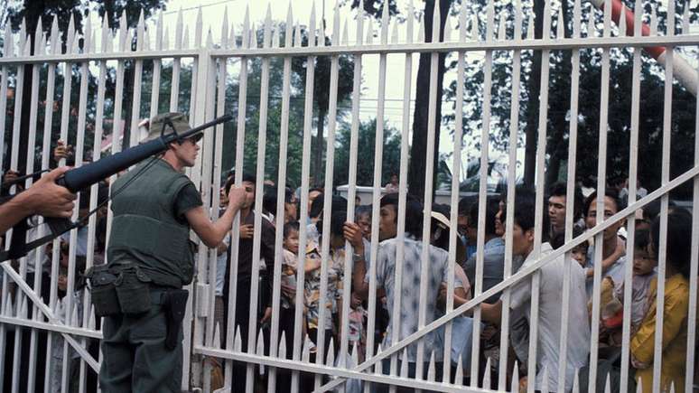 Fuzileiros navais dos EUA vigiam a entrada da embaixada em Saigon, enquanto uma multidão de vietnamitas espera para ser retiradas do país em 29 de abril de 1975