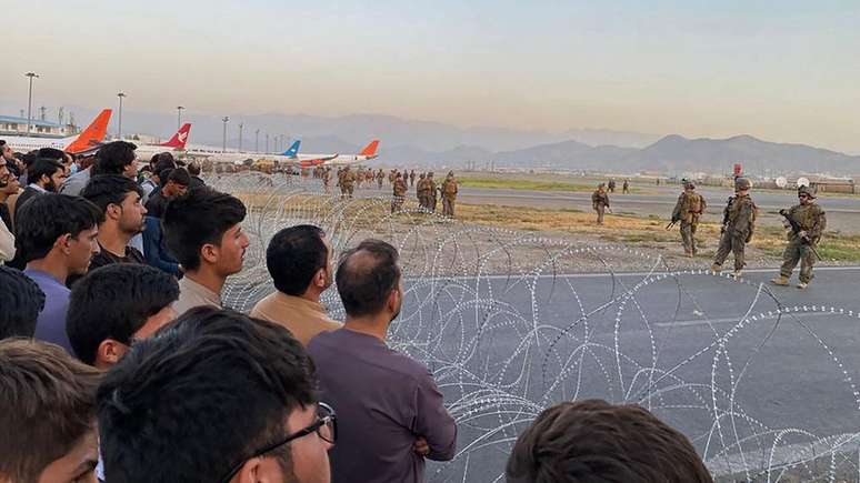 Soldados americanos vigiam o aeroporto de Cabul, enquanto civis são separados por cerca de arame farpado