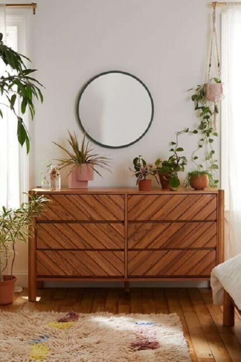1. Cômoda de madeira para quarto decorado com vasos de plantas e espelho redondo – Foto: Urban Outfitters
