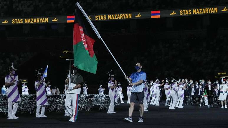 Um voluntário carrega a bandeira do Afeganistão no Estádio Nacional de Tóquio