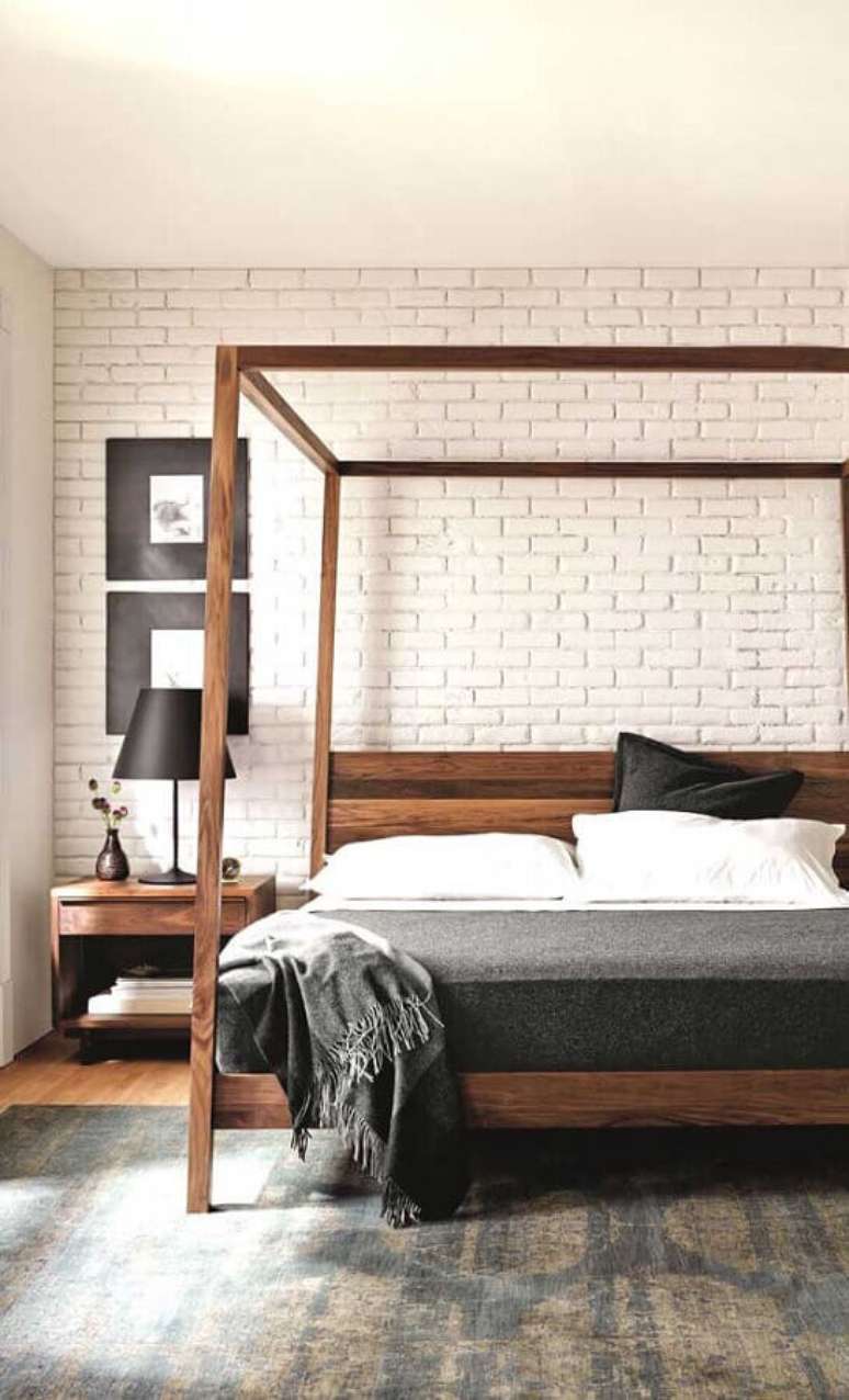 19. Cama com dossel de madeira para quarto de casal decorado com parede tijolinho branco – Foto: DecoRecent
