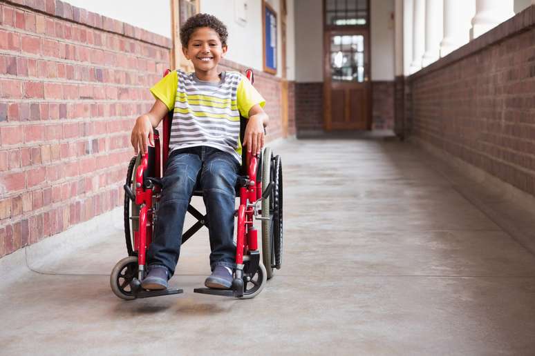 Menino usando cadeira de rodas enquanto sorri para a câmera