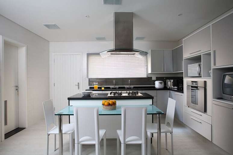 9. Arm&aacute;rio branco para decora&ccedil;&atilde;o clean de cozinha planejada com ilha no meio e bancada de vidro &ndash; Foto: Claudia Arakaki