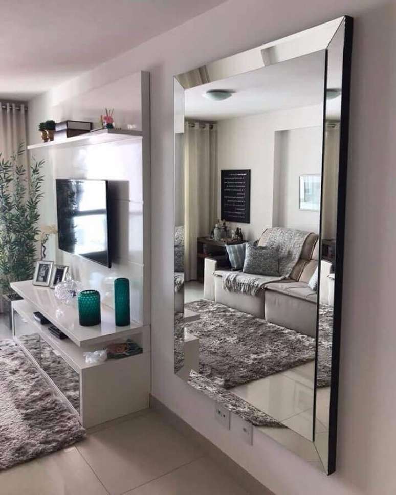 31. Espelho grande na sala de estar branca decorada com tapete felpudo e painel para TV – Foto: Art + Moveis Espelhados
