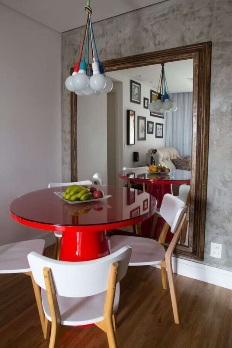 33. Espelho grande na sala de jantar decorada com mesa redonda vermelha e parede de cimento queimado – Foto: Decor Fácil
