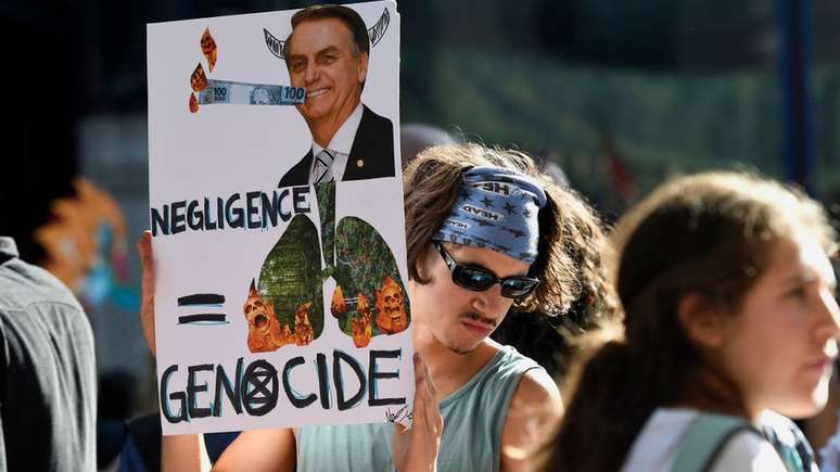 Em Londres, ativista segura cartaz com foto de Bolsonaro e de florestas em chamas, com as palavras 'negligência' e 'genocídio' em inglês