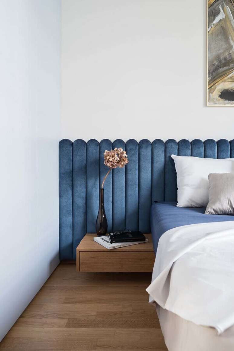 4. Cama com cabeceira almofadada azul planejada para decoração de quarto branco com criado mudo suspenso de madeira – Foto: Dwell