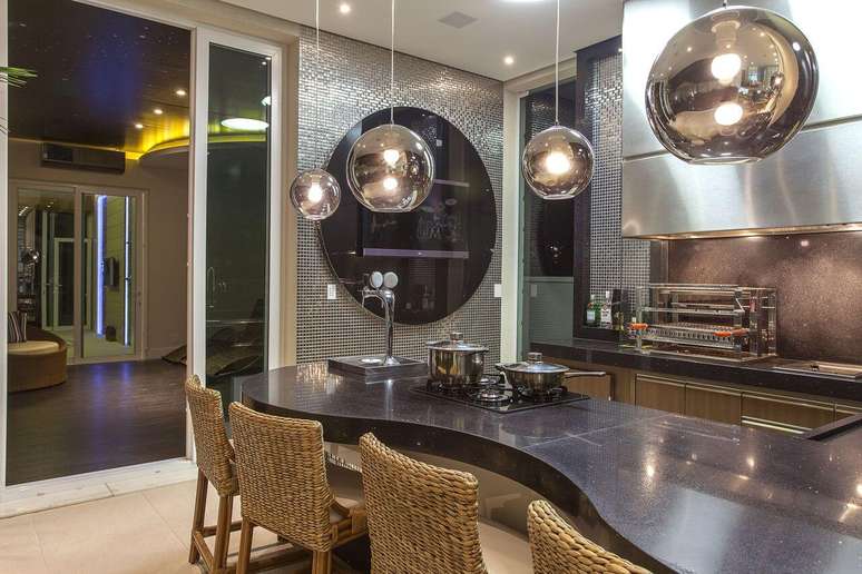 51. Balc&atilde;o de cozinha iluminado com lustre na cor prata e revestimento de pastilha na mesma cor &ndash; Foto Iara Kilaris