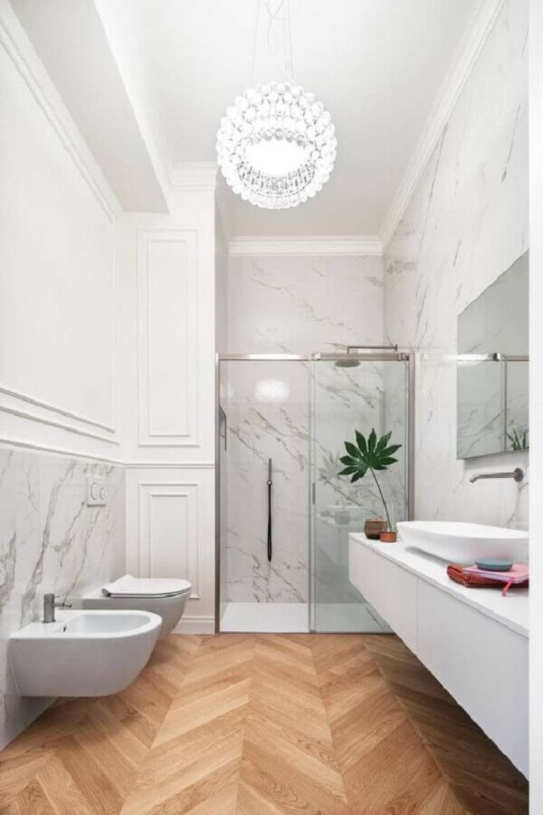 13. Banheiro com piso de madeira decorado com boiserie e meia parede de mármore – Foto: HomeAdore