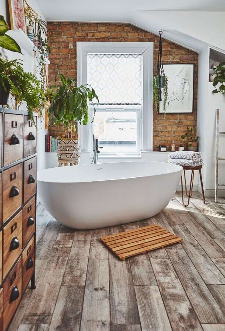 12. Banheira de imersão para decoração de banheiro com piso de madeira e parede de tijolinho à vista – Foto: Real Homes