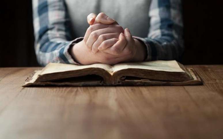 Mãos femininas cerradas sobre a bíblia para que restabeleça sua fé -