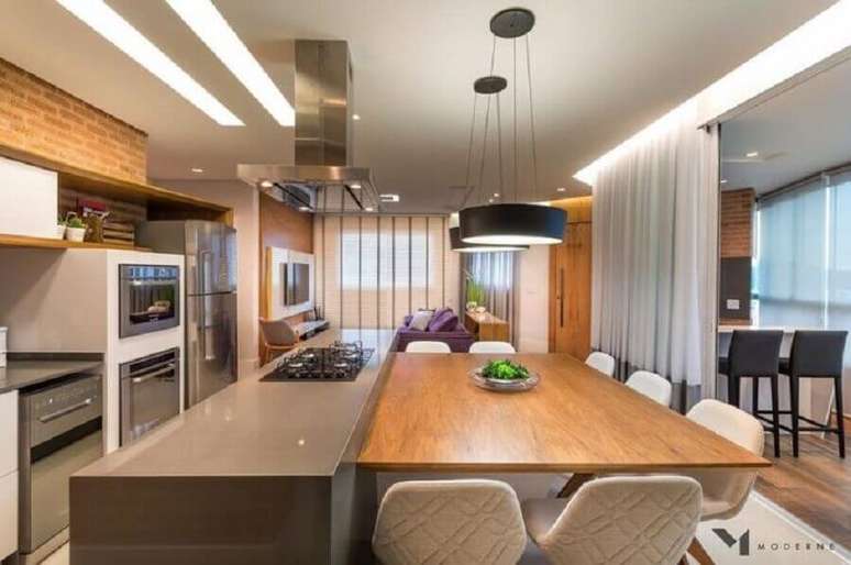 60. Luminária preta para decoração de cozinha com ilha com cooktop e mesa de madeira – Foto: Moderne Arquitetura